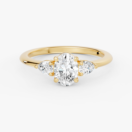 Delphine trestens forlovelsesring med oval diamant og to pæreformede sidesteiner i gult gull, liggende sett forfra
