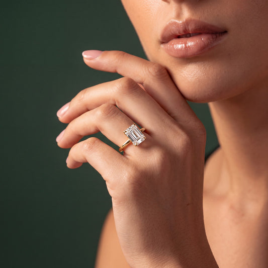 Elara solitaire forlovelsesring med emerald cut diamant i gult gull, båret på hånd